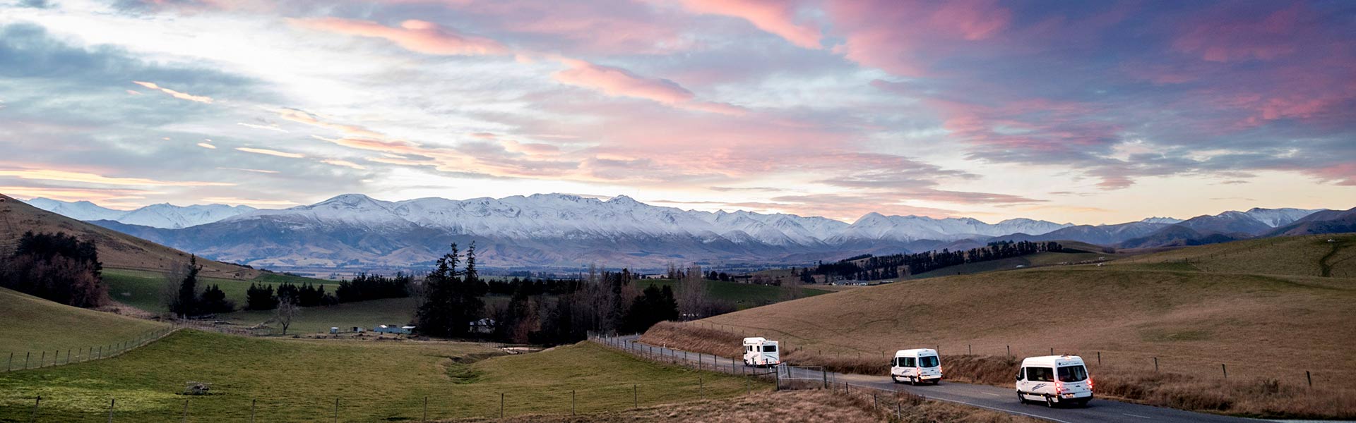 Apollo rental vehicles driving among New Zealand landscape at sunset